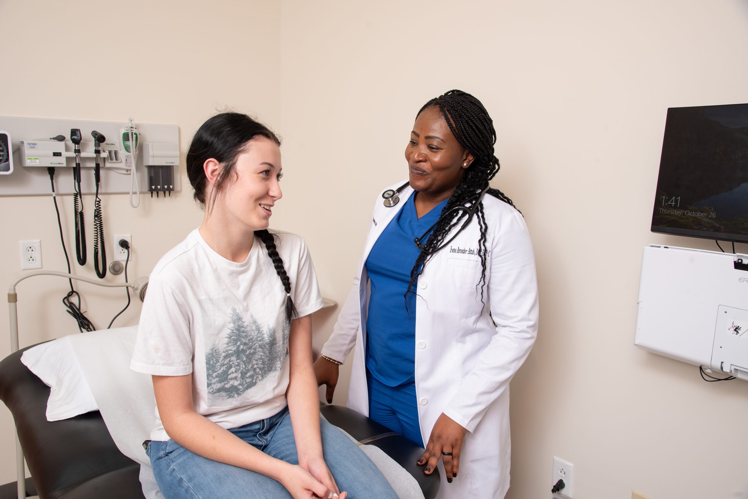 A Chambers Health provider talks with a young adult patient seated on an exam table during a women’s health visit 